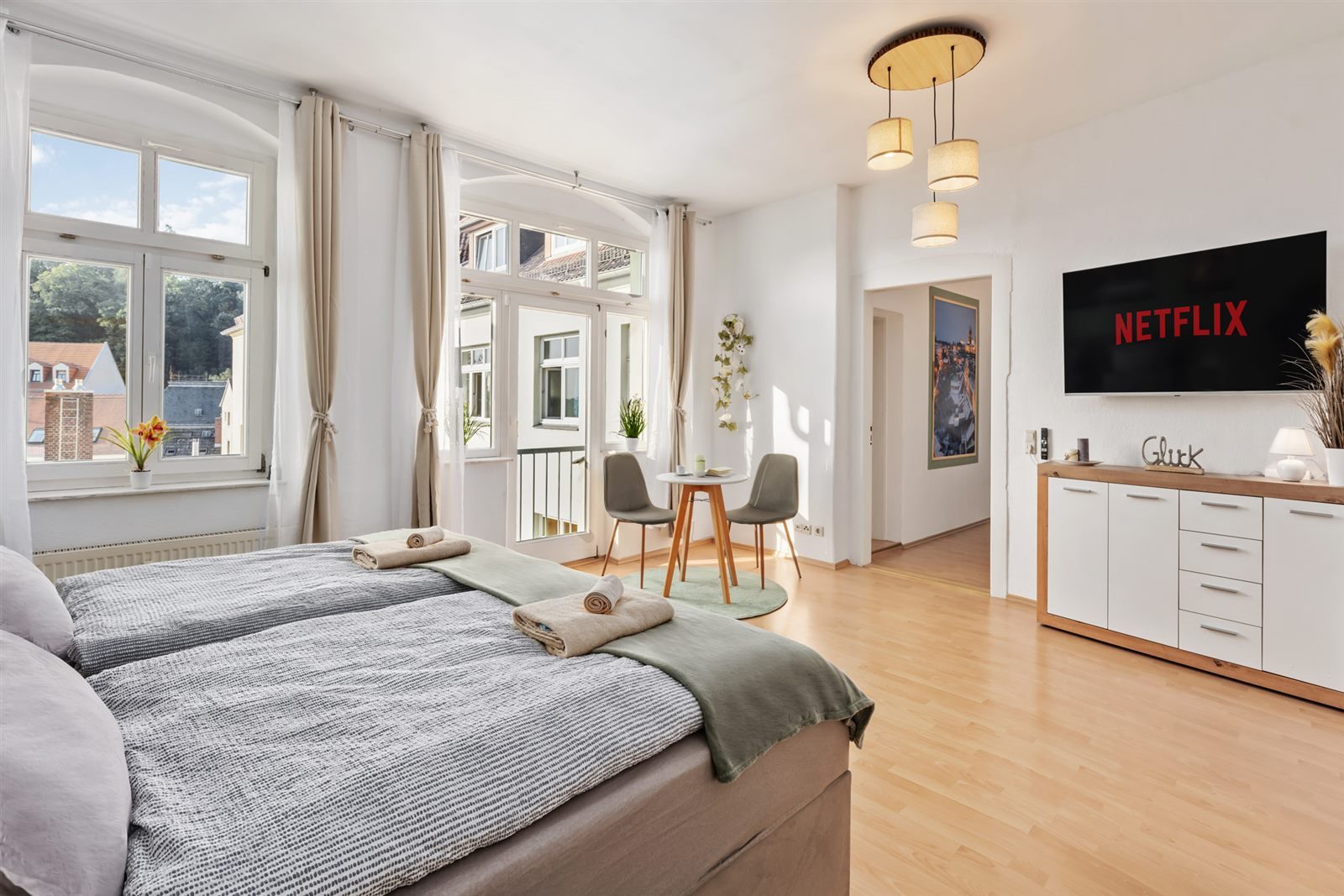 Lichtdurchflutetes Zimmer mit Balkonfenstern und Stadtblick – Tageslicht, Sitzecke und Smart-TV für entspannte Stunden