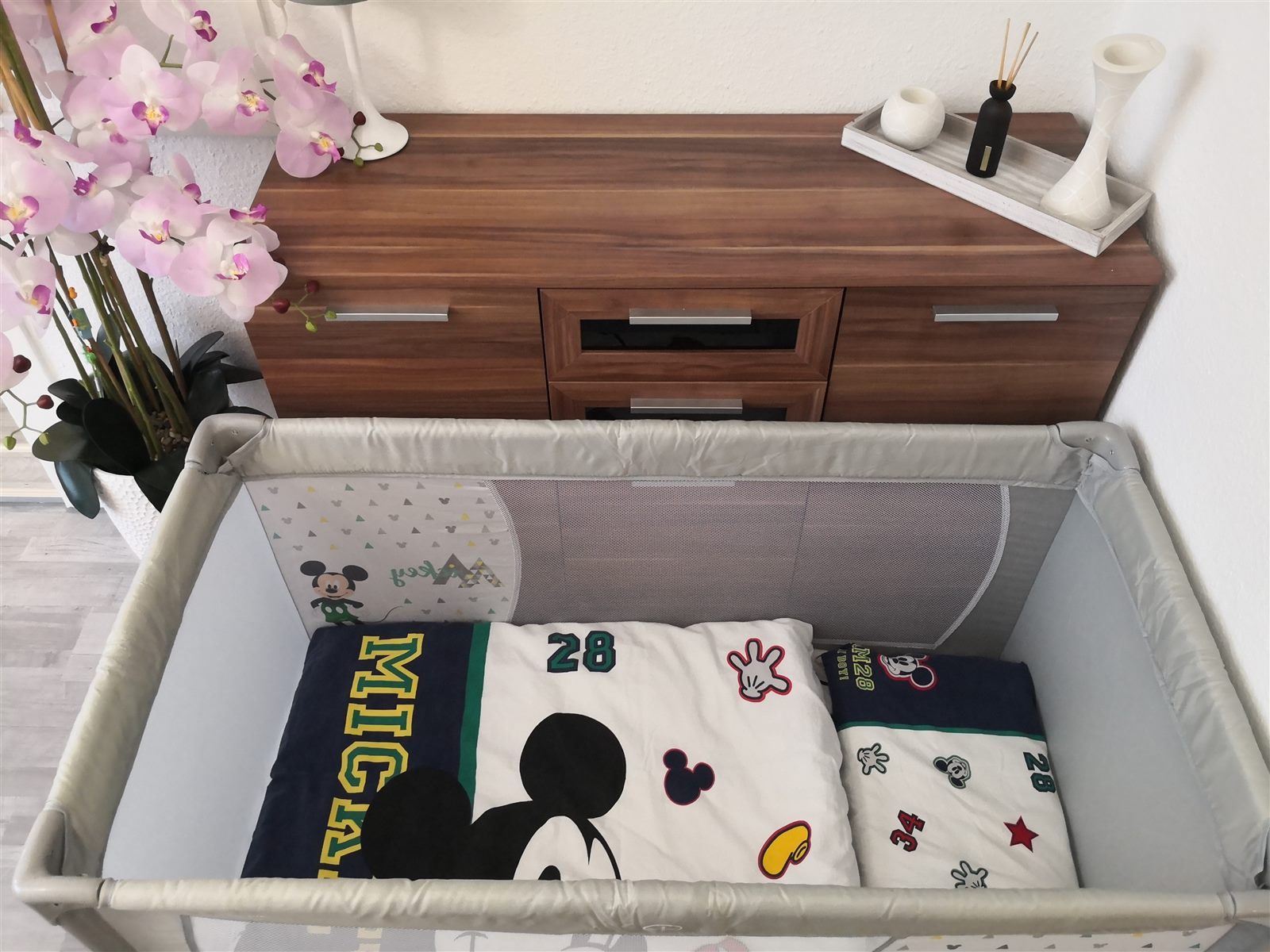 Reisebett mit fröhlicher Mickey-Maus-Bettwäsche vor dem Sideboard – auch die kleinsten Gäste sind herzlich willkommen